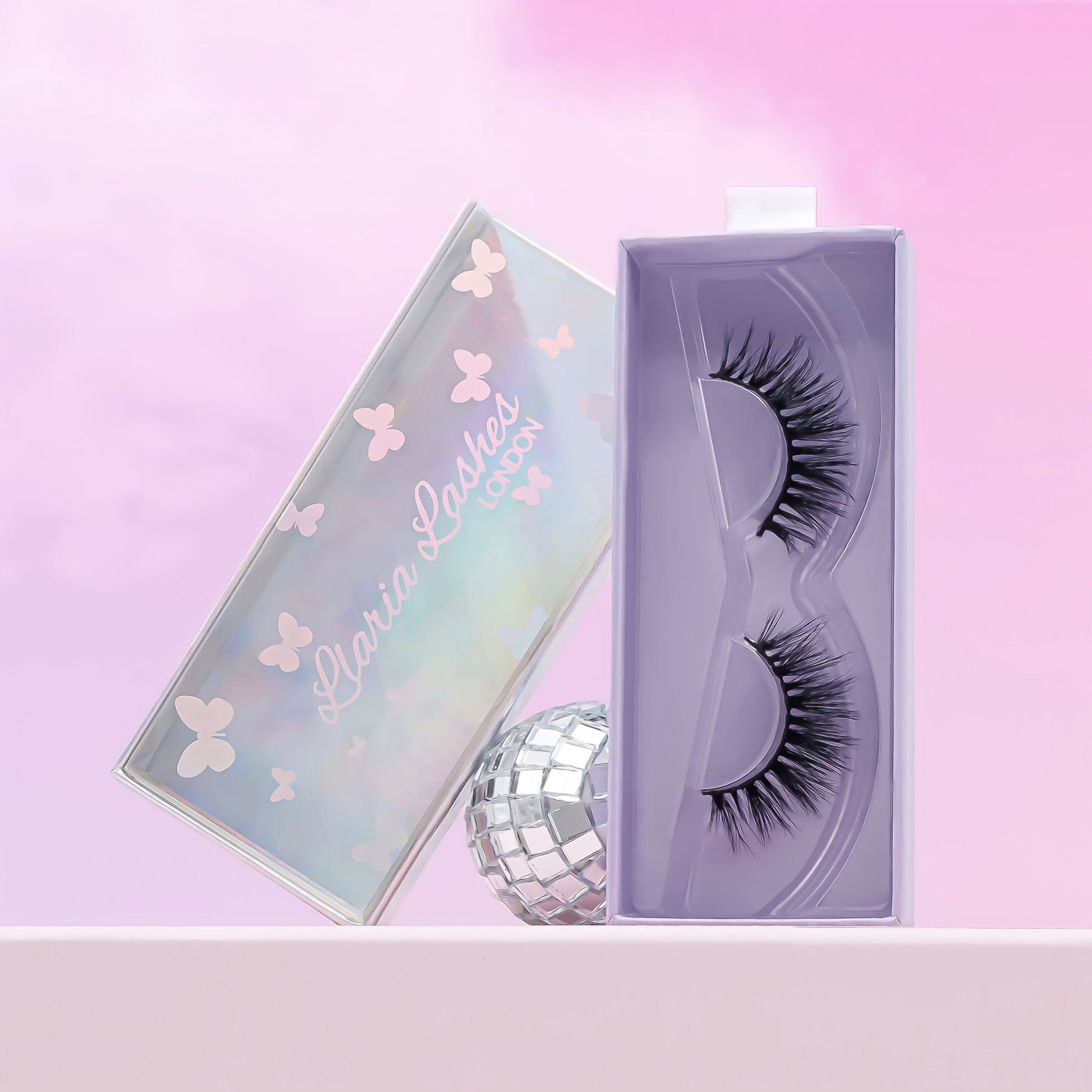 Wispy long and bold false strip eyelashes in purple lash box with disco ball in background.
